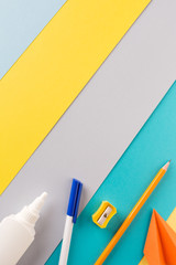 school supplies on bright striped background. minimum set in yellow, blue, grey and orange color: pen, pencil, sharpener, glue. concept: back to school, minimalism. Flat lay, top view, copy space