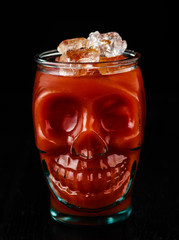 Traditional cocktail Bloody Mary with ice in a skull glass on black table.