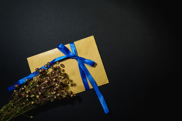 Brown envelope tied with a blue ribbon with dried flowers on a black background