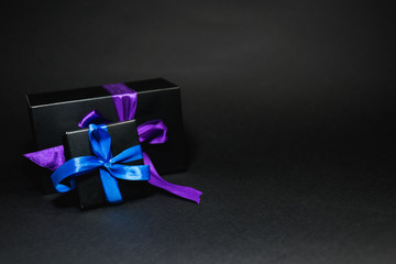 black boxes tied with purple, blue ribbon on a black background