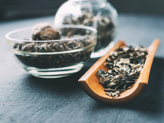 Dry green tea leaves on a wooden spoon and in a glass jar on a dark background.