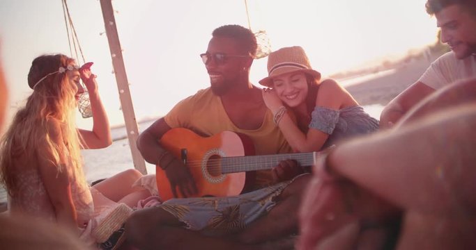 Young multi-ethnic hipsters listening to acoustic guitar at beach party