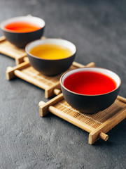 Set of different herbal and fruit teas in clay bowls on bamboo stands. Dark moody.Dark stone concrete background.