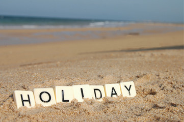 Letters of holiday on a sunny beach with sea in background.