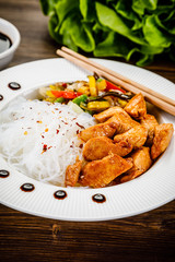 Roasted meat, rice noodles and vegetables on wooden background