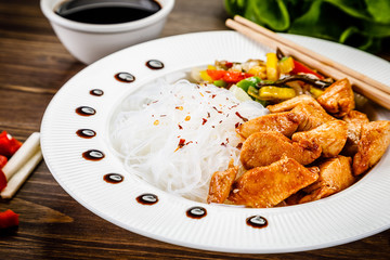 Roasted meat, rice noodles and vegetables on wooden background