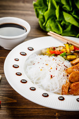 Roasted meat, rice noodles and vegetables on wooden background
