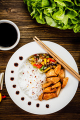 Roasted meat, rice noodles and vegetables on wooden background