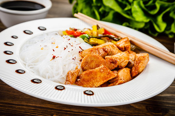 Roasted meat, rice noodles and vegetables on wooden background