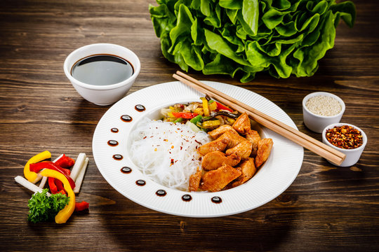 Roasted meat, rice noodles and vegetables on wooden background