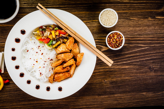 Roasted meat, rice noodles and vegetables on wooden background