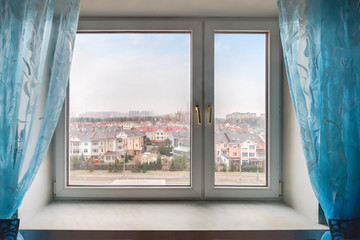 Fototapeta na wymiar Home window with blue curtain and view to residential suburban building exterior on blue sky background.