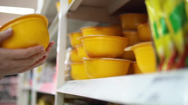 Someone chooses and buys yellow containers with noodles or instant soup in a supermarket in the snacks department.