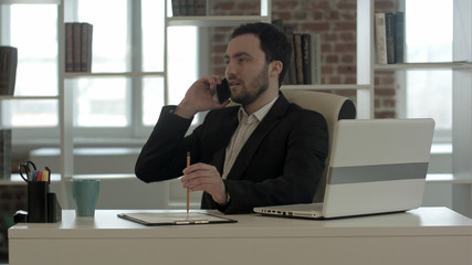Man talking on mobile phone while using laptop computer