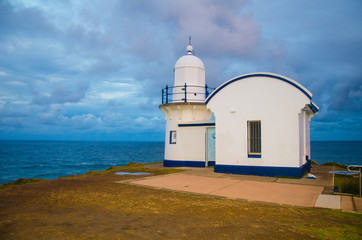 Fototapeta na wymiar Old historical small lighthouse on top of the hill overlooking pacific blue ocean during sunset cloudy sky for honeymoon family friends holiday in Australia