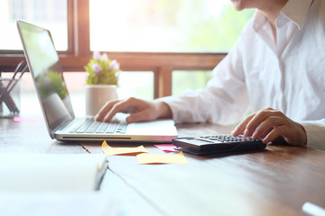 Man calculate finance business using calculator and computer laptop analysis data at morning time in modern office.