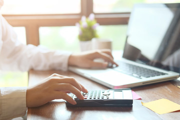 Man calculate finance business using calculator and computer laptop analysis data at morning time in modern office.