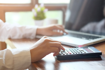 Man calculate finance business using calculator and computer laptop analysis data at morning time in modern office.