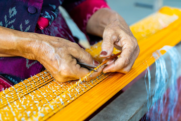 Thai Woman Making Ties Mudmee Board Weaving or Ikat Thai Silk Pattern Weaving on Small Red Weaving Mill Before Bring to Tie and Dyed