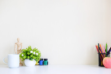 Mockup table with plant decorate, cup of coffee, water colour, jar of colour pencil and wooden model artist workspace.