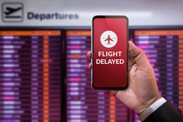 Modern Technology in Travel Concept. Flight Delayed on Smartphone Screen. Businessman using Mobile Phone in front of Departures Board to Re-Checked Flight Information in Airport © blacksalmon