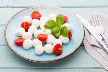 Delicious caprese salad with ripe cherry tomatoes and mini mozzarella cheese balls with fresh basil leaves.