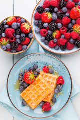 Homemade waffles with berries salad on blue dishes. Vintage wooden background.