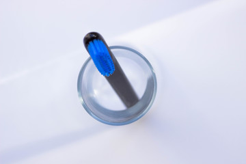 Black style toothbrushes  wiht blue bristle in glass on table on lwhite moning background, top view