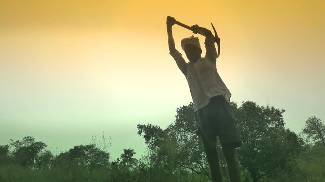 A slow motion shot of an Indian farmer digging up fertile soil in his farm with pickaxe or Mattock to sow seeds. An Indian middle aged farmer digging his farmland with pickax. Indian national flag 