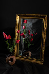 Abstract Magic. Tulip flowers in dark room reflecting in mirror with gold baguette