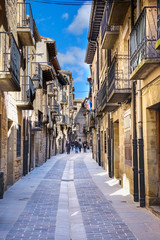 Fototapeta na wymiar Main street of the town called Mayor with facades of stone houses and iron balconies typical of northern Spain and people passing through it. Stone paving floor