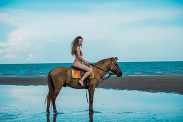 Fototapeta na wymiar Pretty young lady riding a horse on the beach background of the sea