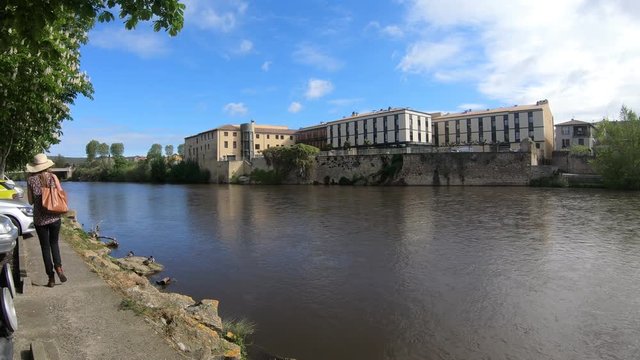 Young woman with a hat and a handbag photographing with her smartphone and strolling along the river Aude in the French town of Limoux, Languedoc in the south of France