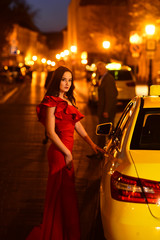 Luxury woman in evening dress at night city go to prom on taxi. luxury woman in red dress wait taxi.
