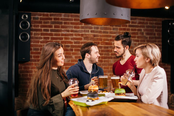 Young friends having a great time in restaurant. Group of young people eating various kinds of burgers and chatting about everything in popular dining place.