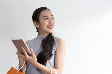 Fototapeta premium Happy young woman holding shopping bags and mobile phone. Makes online shopping on a tablet.