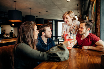Group of young colleagues adults friends drinking beverages, blonde woman making a toast in a restaurant