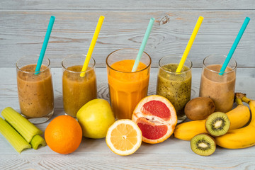 Five glasses of smoothies with straws and various fresh fruits around