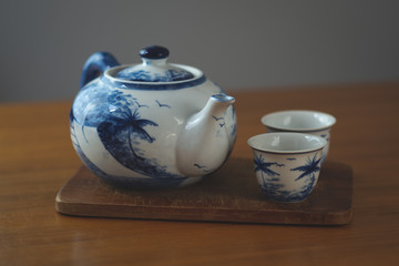 Blue and white china teapot with two matching cups resting on a wooden board on a table with a rustic feel