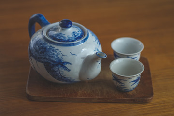 Blue and white china teapot with two matching cups resting on a wooden board on a table with a rustic feel