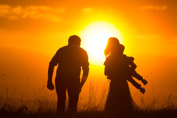Parents with a baby in summer sunset meadow - silhouette