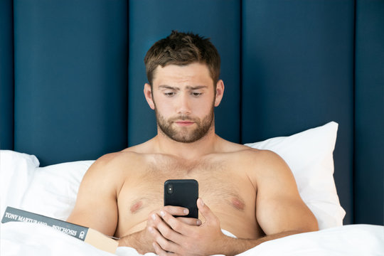 Shirtless Sexy Hunky Man With Beard Lies Naked In Bed Using Mobile Phone