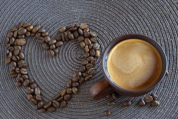 Cup of hot coffee and coffee grains in form a heart. Kind from above