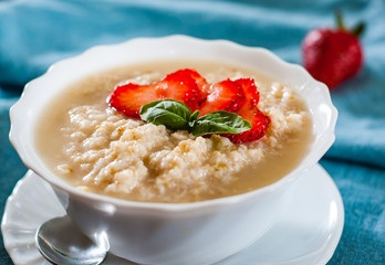 Oatmeal porridge with strawberries in bowl on table