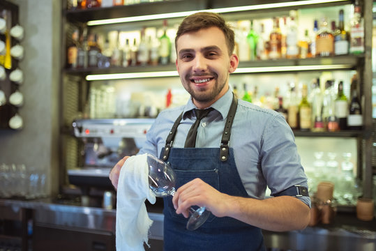 The happy bartender cleaning the glass on the bar