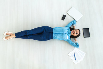 The happy businesswoman laying on the floor near gadgets and papers
