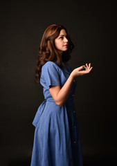 3/4 portrait of brunette lady wearing blue dress. posed on black studio background.