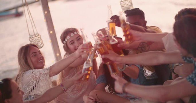 Young multi-ethnic hipster friends toasting with beer at beach party
