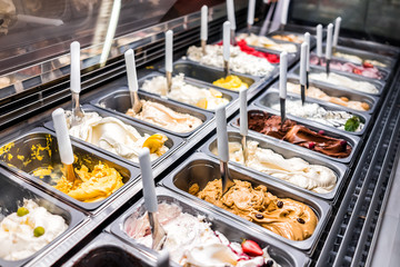 Ice cream frozen yogurt colorful serving counter parlour with many scoopable flavors, sorbet, chocolate, toppings, coffee - Powered by Adobe