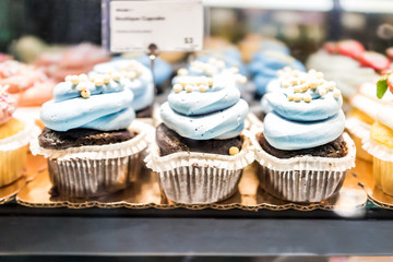 Macro closeup of chocolate cupcakes on display in bakery in muffin paper liners with blue blueberry icing cream
